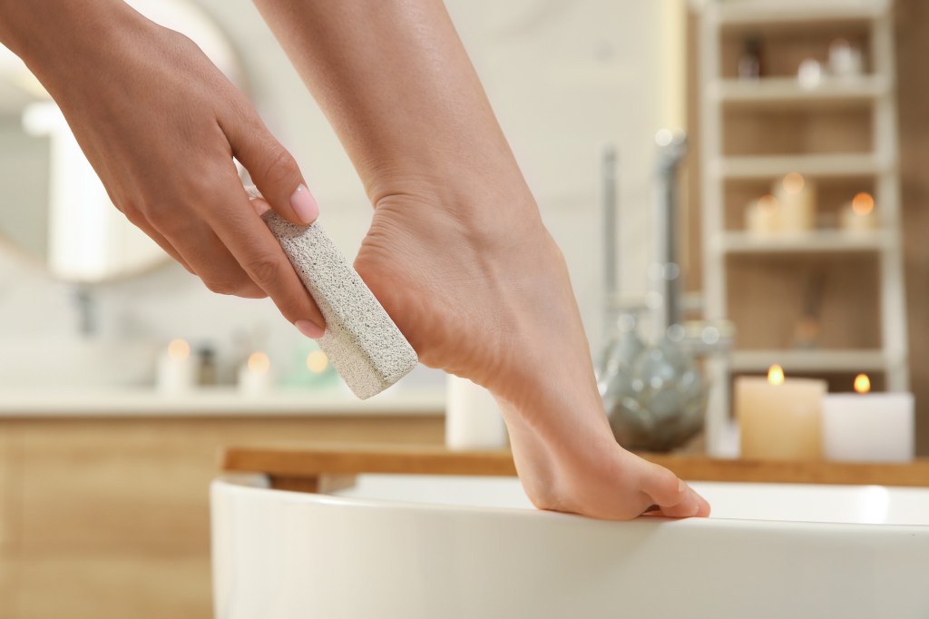woman exfoliating feet with pumice stone for at home pedicure