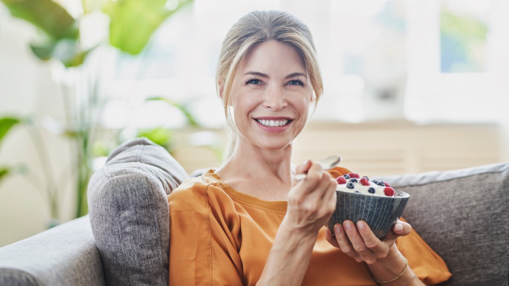 A woman in a gold top eating a bowl of yogurt topped with berries for constipation