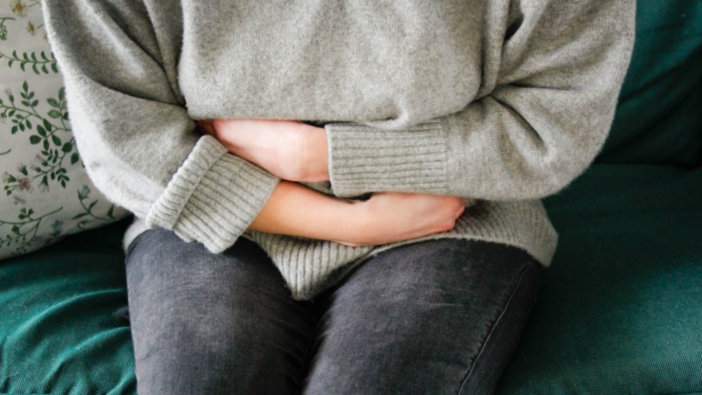 A woman in a grey sweater clutching her stomach while dealing with constipation