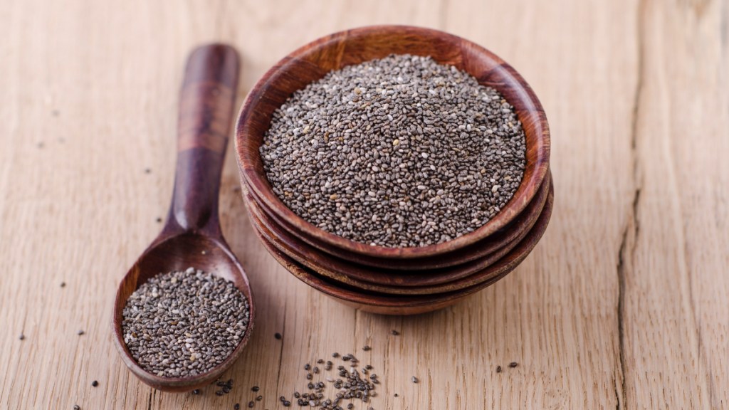 A bowl of chia seeds next to a spoon of chia seeds on a table