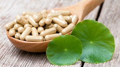 Gotu kola leaves next to supplements in a wooden spoon