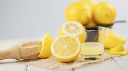 A glass of squeezed lemon juice and lemons around