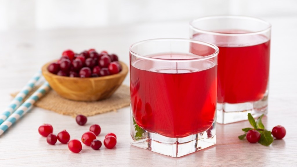 Two glasses of cranberry juice on a table beside a bowl of fresh cranberries
