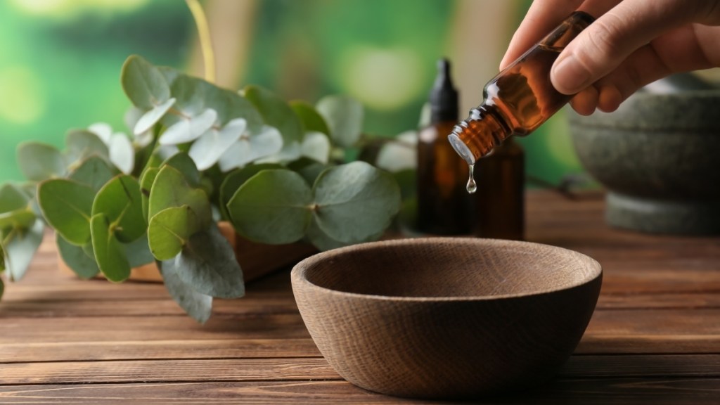 Eucalyptus essential oil, which has many health benefits, being poured into a wooden bowl from an amber vial