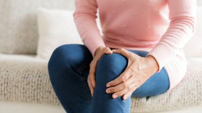 Bottom half of woman holding her knee in pain
