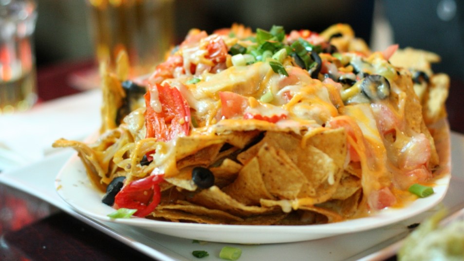 cheesy nachos on a white plate with tomatoes, jalapenos, and olives, a mood-lifting food