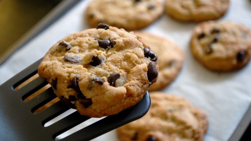 freshly baked chocolate chip cookie on a spatula, with other cookies in the background
