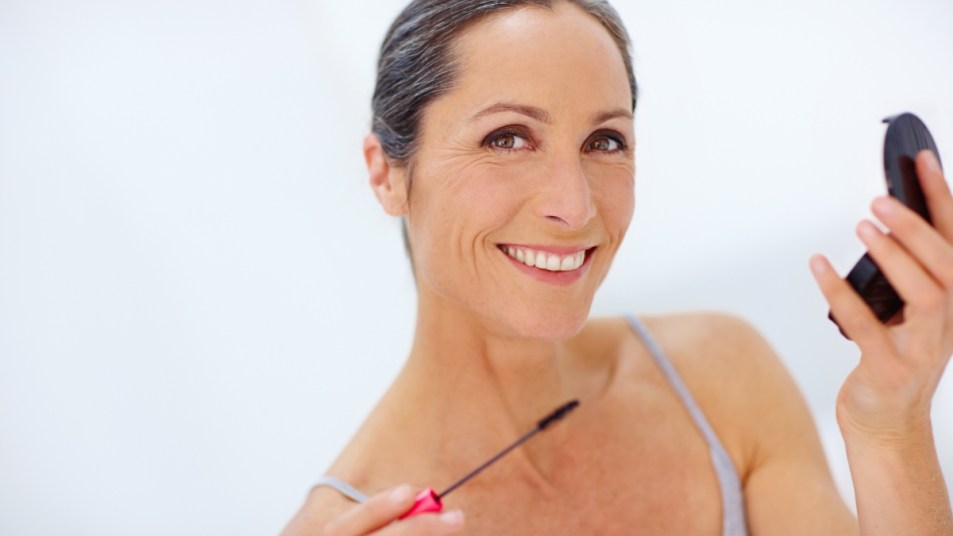 mature woman smiling and holding mascara, concept for fuller brows and lashes