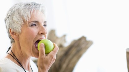 mature woman with short gray hair biting into a green apple