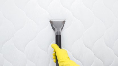 hand in yellow protective glove vacuuming modern white mattress