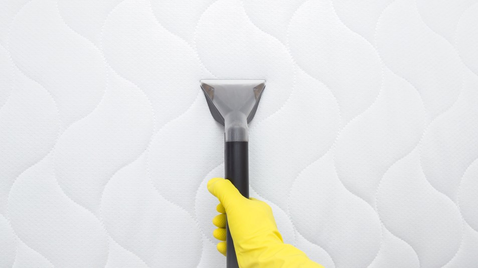 hand in yellow protective glove vacuuming modern white mattress