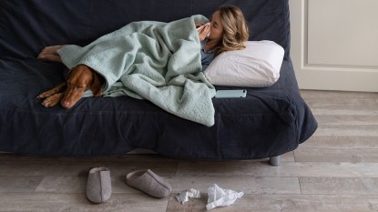 Sick woman at home lying on a futon with her Vizsla dog, suffering from flurona