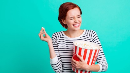 Young woman eating popcorn and looking very happy because her mood is boosted via serotonin