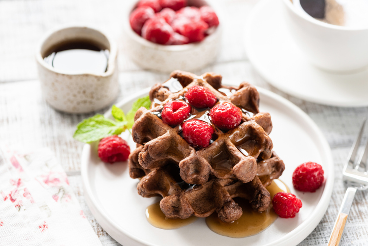 chocolate brownie waffle made in a waffle iron. topped with raspberries and syrup.