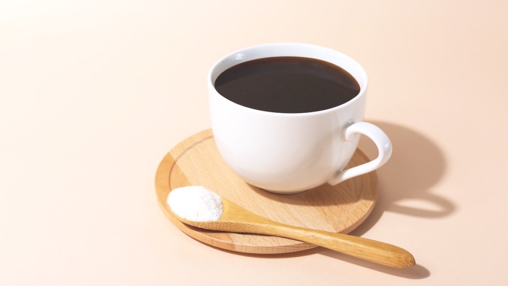 A cup of coffee on a wooden tray next to a wooden spoon with collagen, which helps nails with dents grow out.
