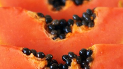 Bright orangeBright slices of papaya fruit lined up in a row with black seeds showing.