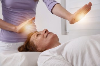 Mature woman lies on a table while receiving healing reiki session.