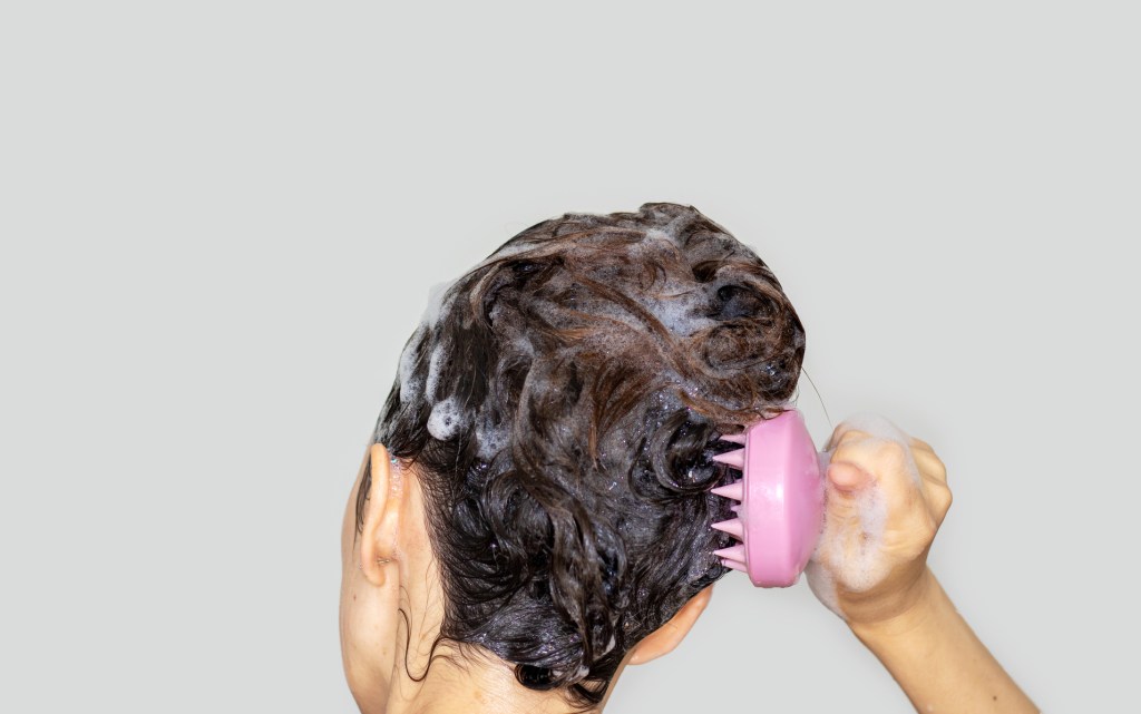 woman using scalp brush to exfoliate hair while shampooing