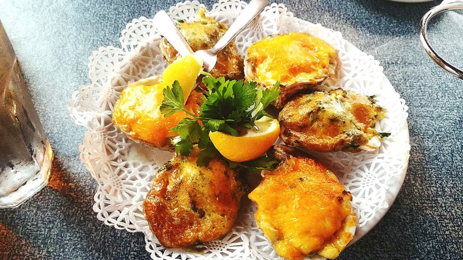 A tray of Oysters Rockefeller arranged on a plate with a lemon and herbs in the middle.