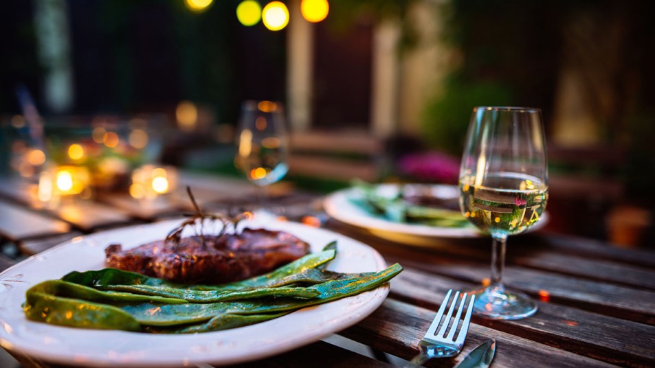 A glass of white wine sits next to a plate with bright green beans and a steak.