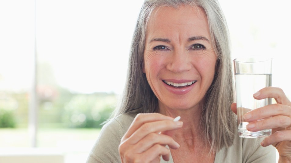 Mature woman taking a pill that represents SpiceFruit, holding glass of water, smiling