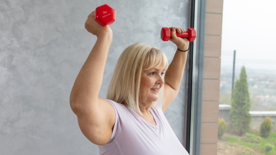 mature white woman holding two red dumbbells, completing a strength training workout