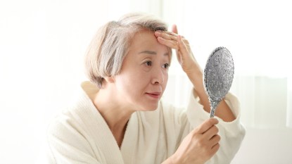 mature woman looking at her skin in the mirror, concerned