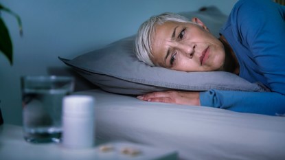 mature woman lying in bed, staring at sleep supplements and water on table
