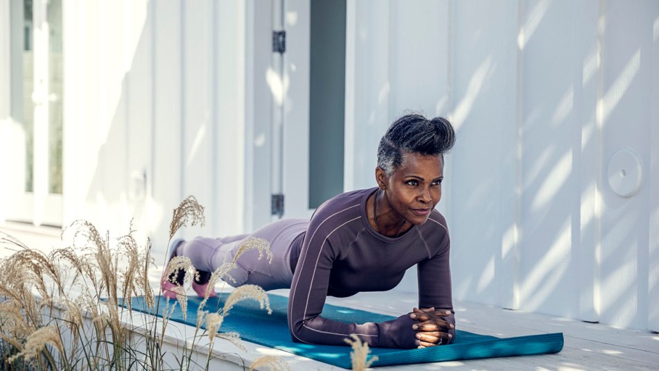 Mature black woman wears a purple outfit while holding a perfect plank yoga pose on a teal yoga mat