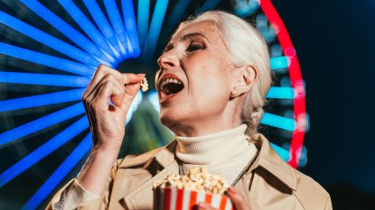 Woman with white hair eating popcorn with a lit up ferris wheel in the background.