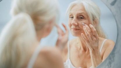 mature woman in front of mirror applying face cream