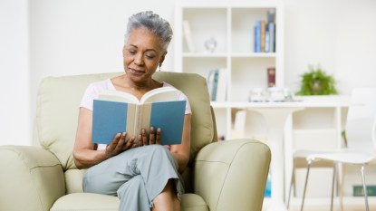 mature woman smiling and reading a book in a comfortable chair
