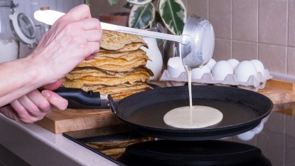 Woman's hands making pancakes in frying pan on stovetop