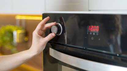 Woman about to switch on broiling setting on a oven after learning how to preheat an oven quickly