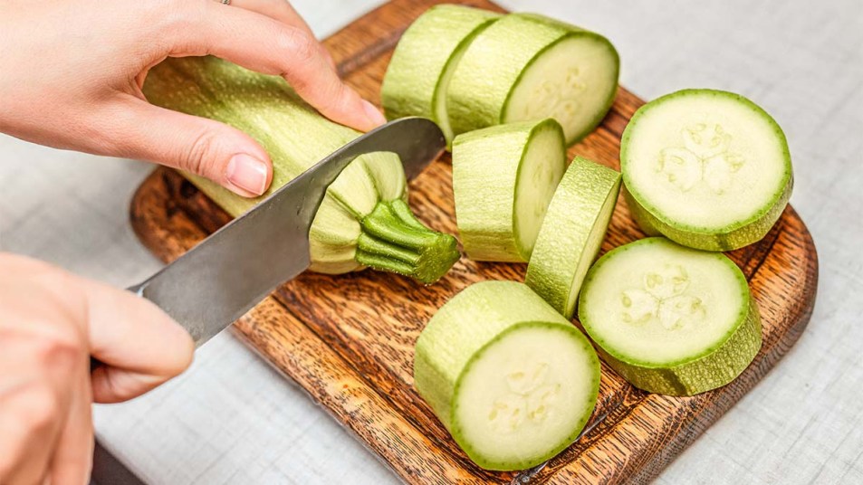 A-woman-slicing-a-zucchini-on-a-wooden-cutting-board-in-a-roll-cut-pattern