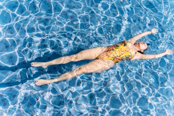 Woman in a swimsuit floating in a blue pool on a sunny day
