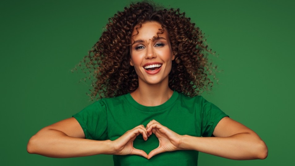 Smiling, healthy woman in a green shirt holding her hands in a heart shape