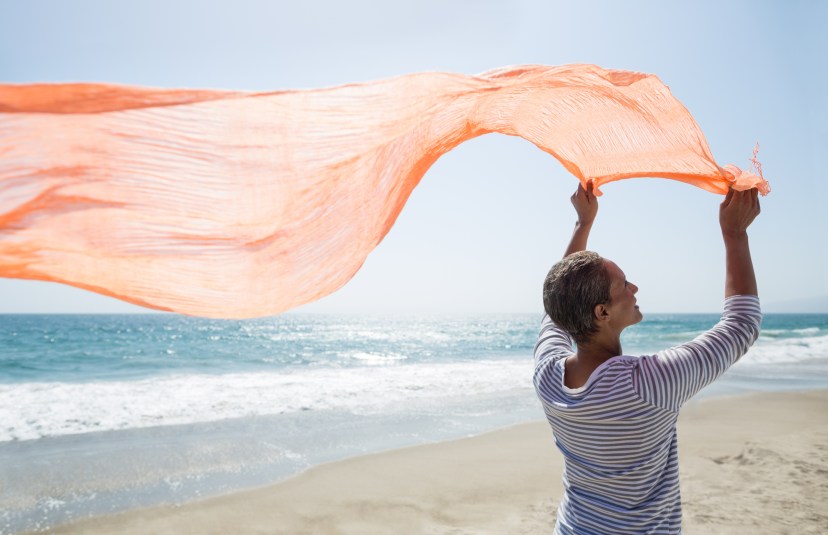 Senior woman standing on beach holding scarf