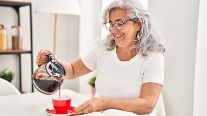 Woman-pouring-drip-coffee-into-a-red-mug-while-sitting-in-her-breakfast-nook