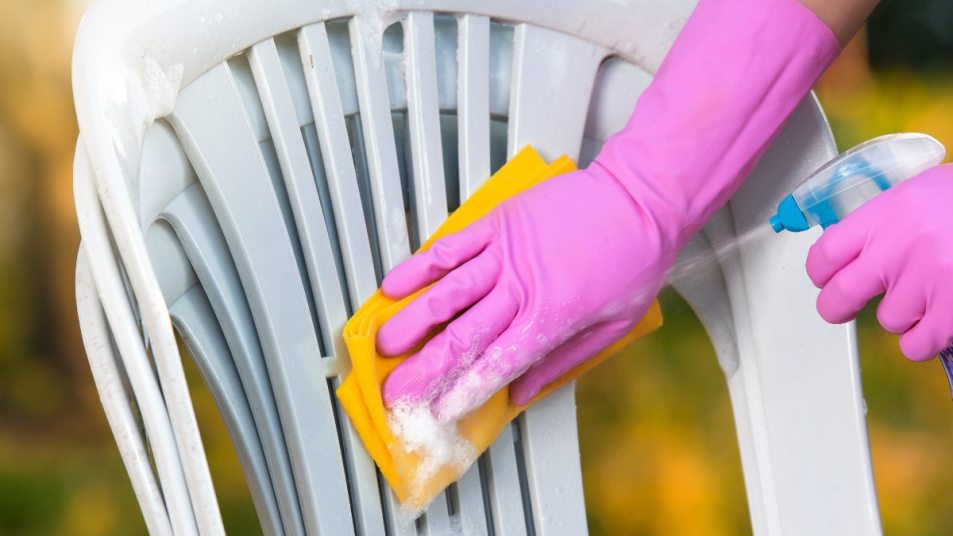 close up of hand in a pink glove spraying white plastic outdoor furniture, using yellow cloth