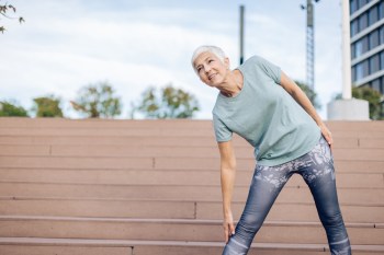 Older woman doing a hip stretch outside