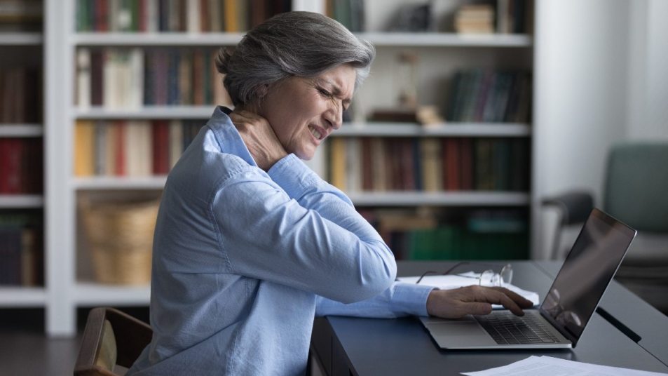 mature woman rubbing sore neck, poor posture sitting at laptop