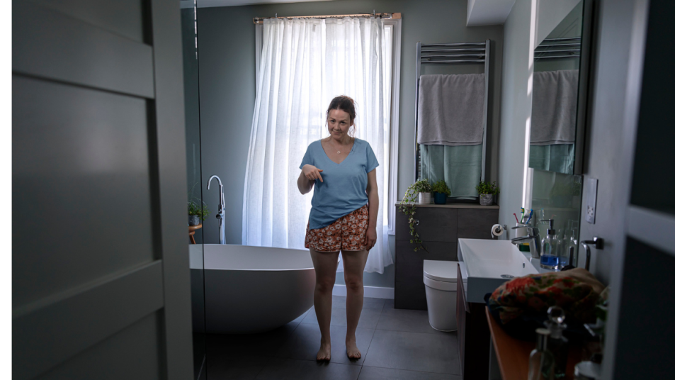 Woman Stands In Bathroom In T-shirt and Briefs and Points at Briefs With Concern Over Bladder Leaks and Bladder Protection
