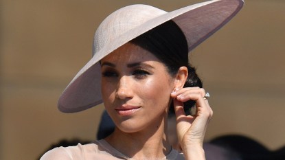 Duchess of Sussex Meghan Markle in white hat slightly tilted with hand to her ear