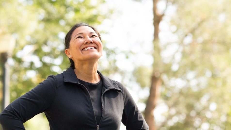 mature woman in workout gear outdoors, smiling and looking upward, weight loss concept