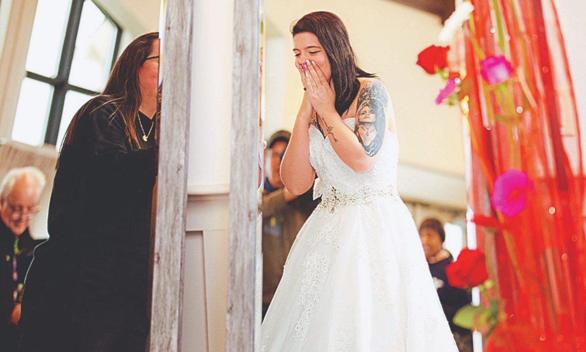 military bride gazing into a mirror, hands over mouth, smiling, wearing a wedding dress