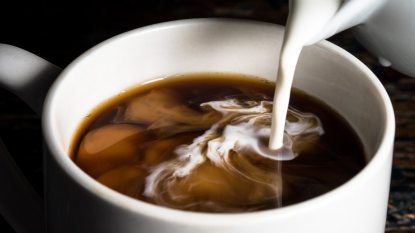 pouring coffee creamer into a white mug of black coffee