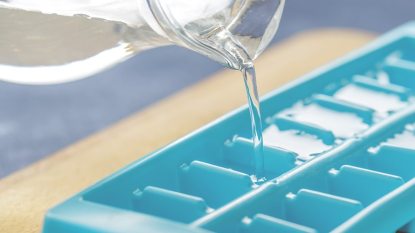 water in a pitcher being poured into blue ice cube tray