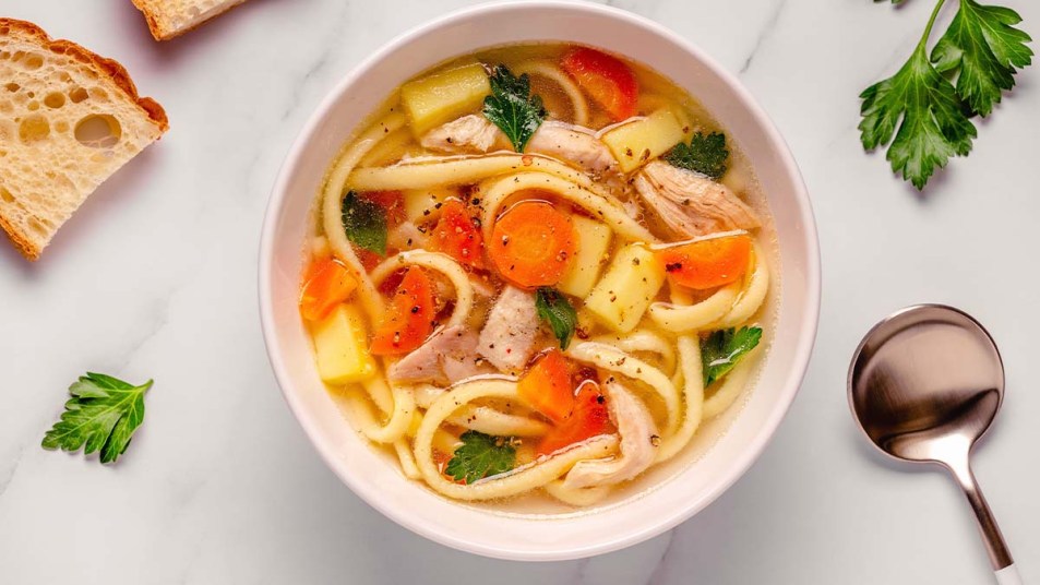 Chicken soup with noodles and vegetables in white bowl
