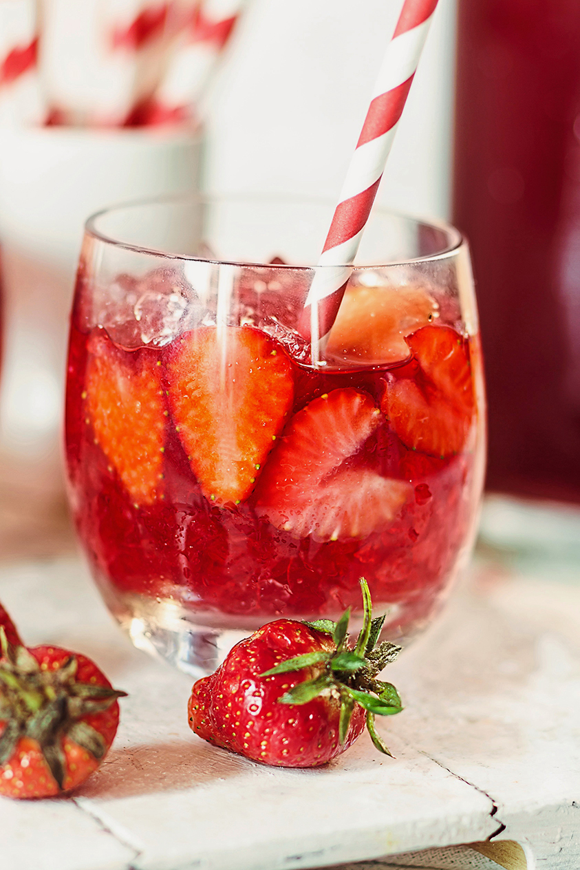 Glass of iced red fruit blacktea with sliced strawberries and crushed ice